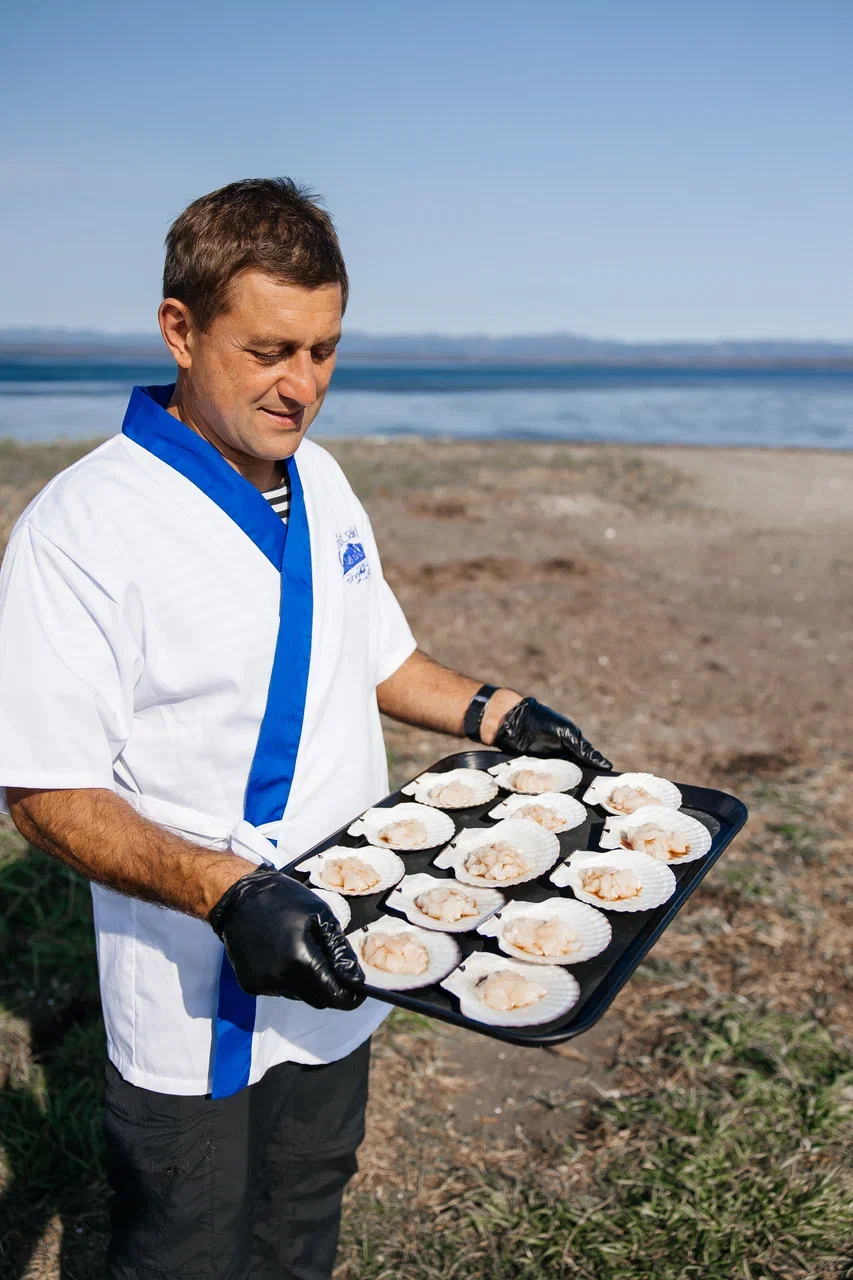 Шеф-повар АМИСТ с подносом запечённых гребешков на берегу лагуны Буссе